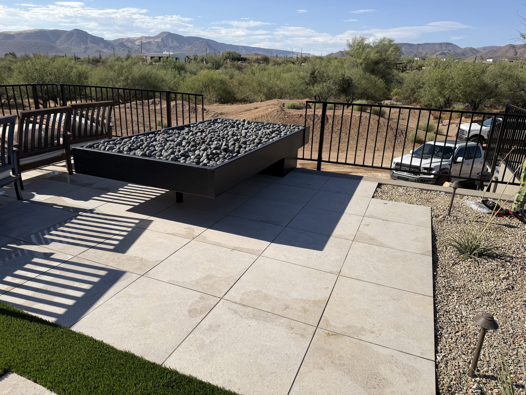 Raised black metal fire pit with rock media on a paver patio — Standard Pools project